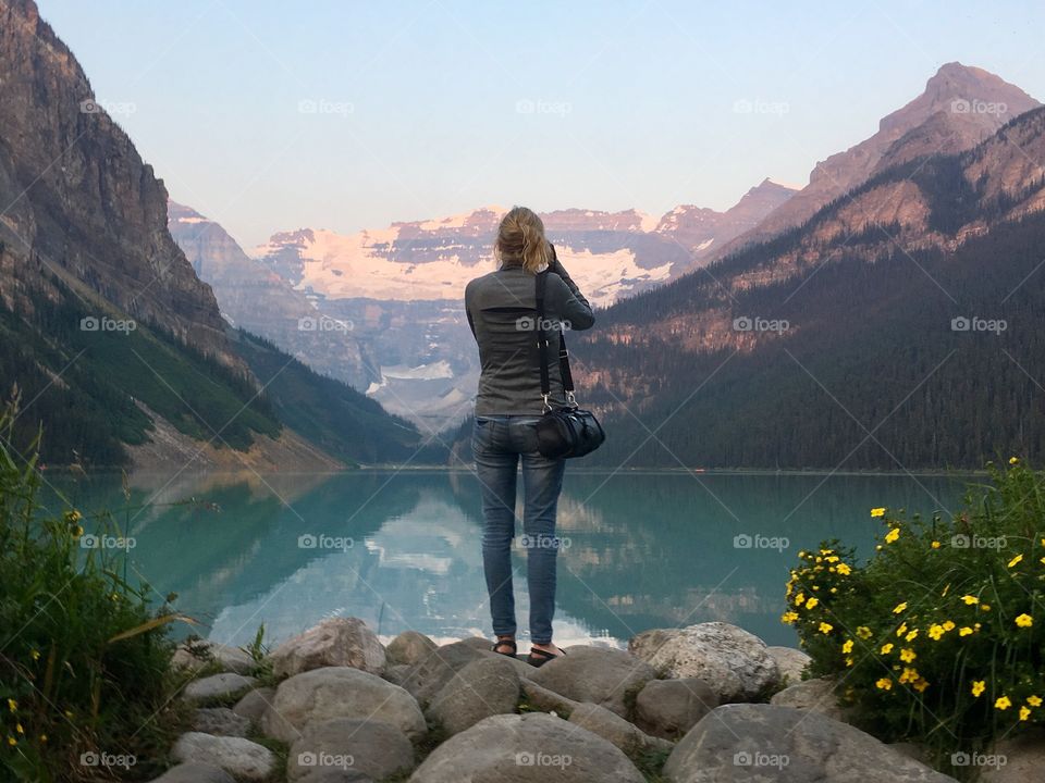 Woman photographing glacial mountain lake 