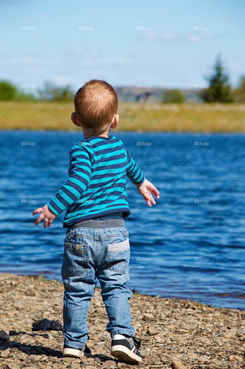 Rear view of a boy standing near lake