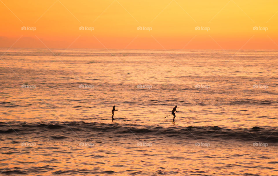 silhouettes of two people paddling in the ocean