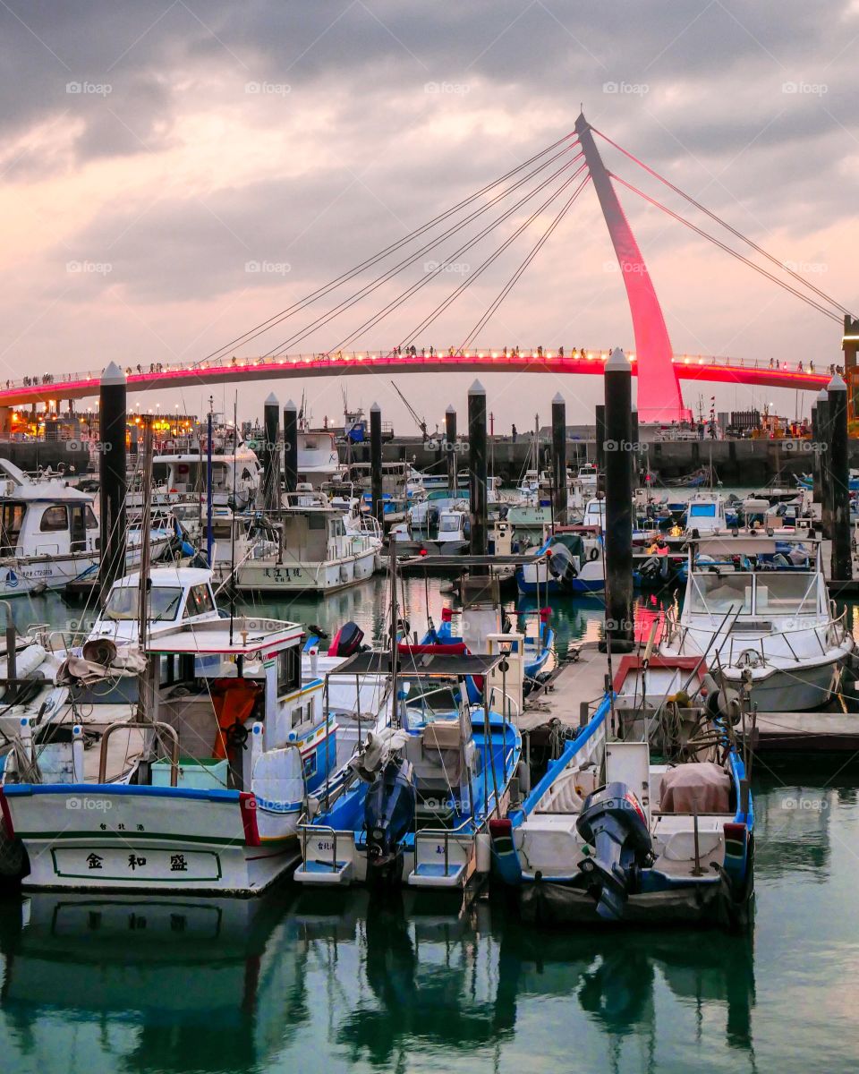 Sundown at Fisherman's Wharf, Lover's Bridge can be seen in the background, along with a soft purple sky . In the foreground some fishing boats sit still on the water.