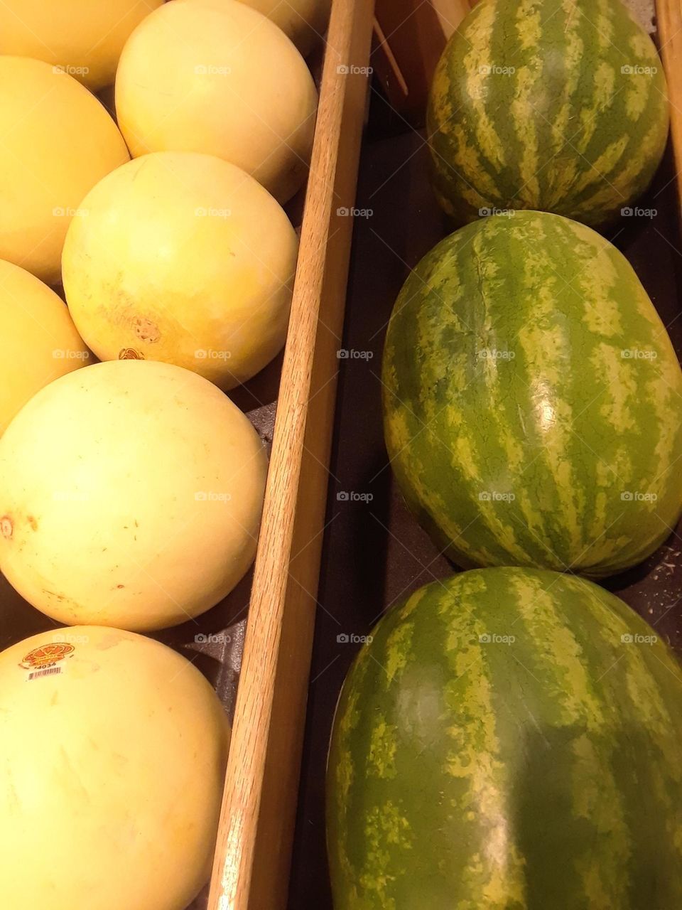 The produce section at a local supermarket, with watermelon on one side and melons on the other, with a divided in between.