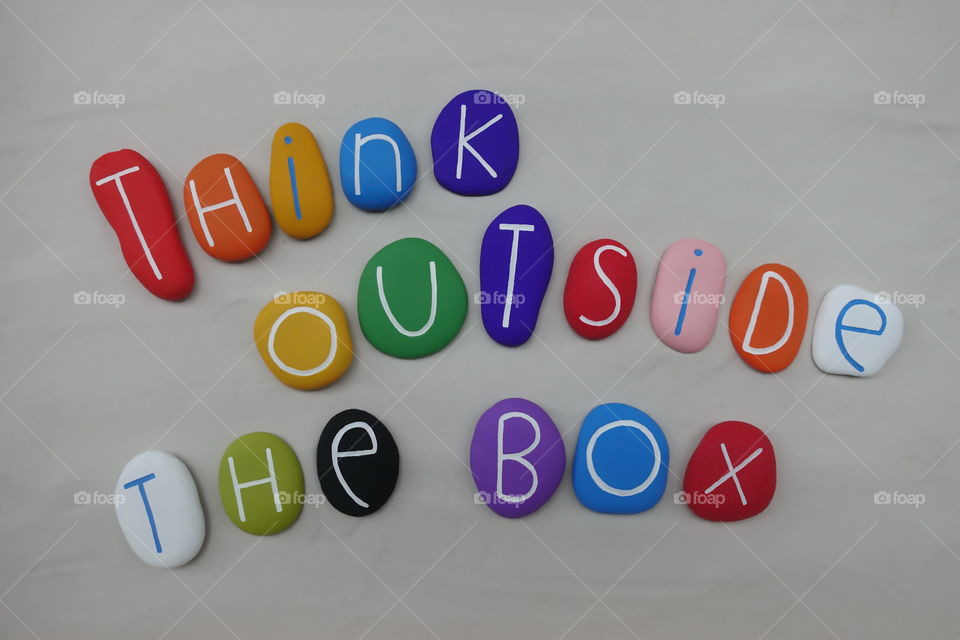 Think outside the box, multi colored text composed with sea stones over white sand