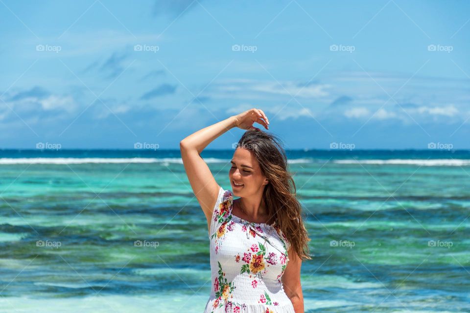 Portrait of happy young woman wearing sun dress standing in front of turquoise ocean