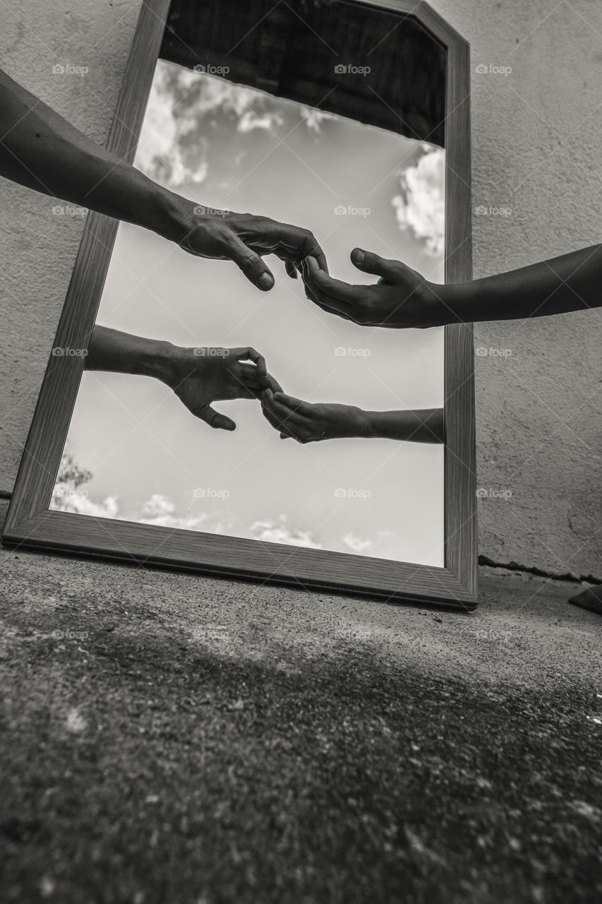 Hands of a female and a child in front of a mirror. Black and white