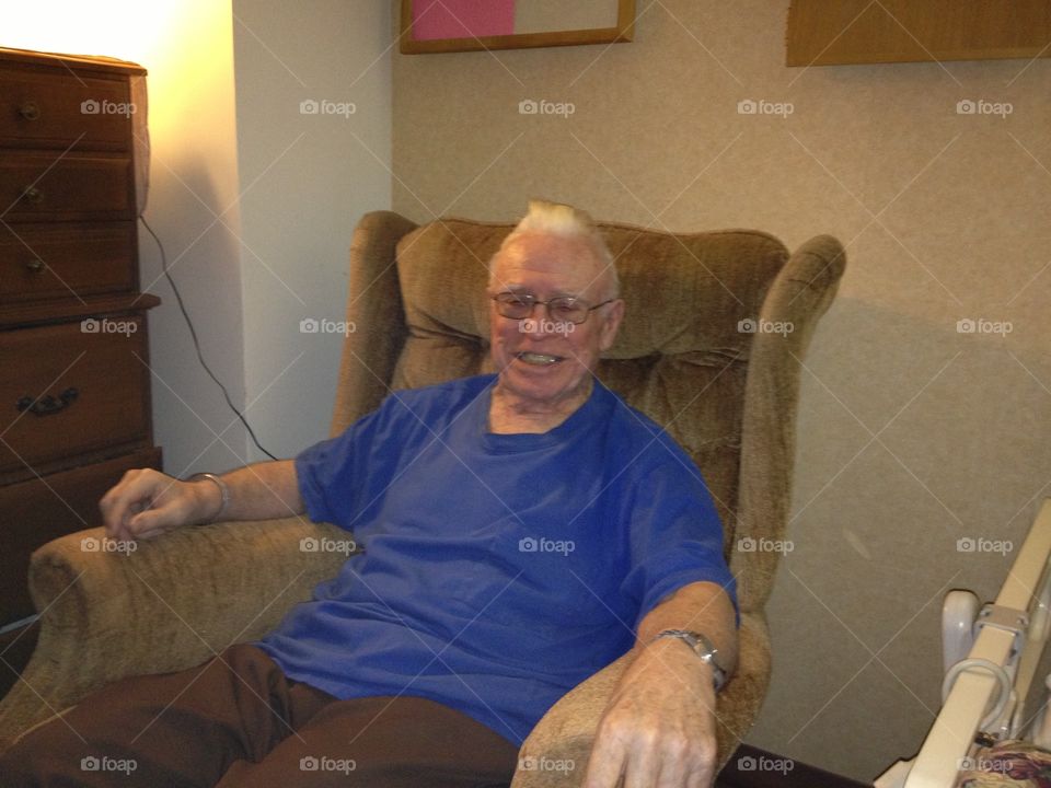 Older man smiling sitting in recliner, eyeglasses on. Senior citizen.