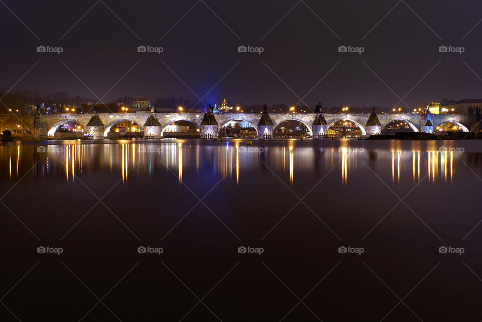 View from the island on an architectural monument of Charles bridge. Long glimpses of night lights and architectural lighting in the broad waters of the Vltava River