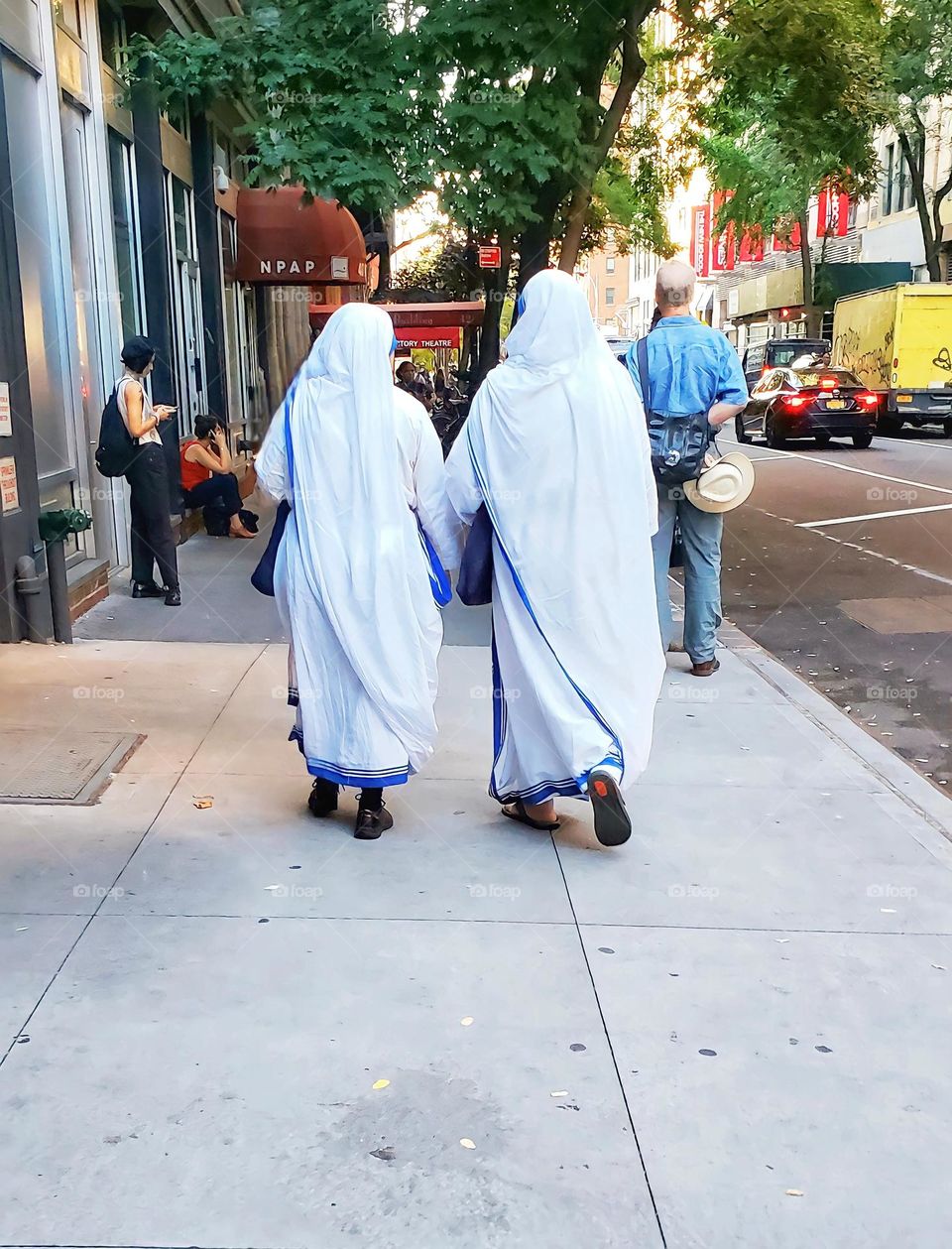 Two muslim women walk down a city street wearing an Abaya and hijab. Their backs are facing towards the camera.