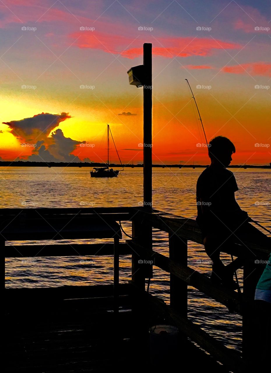 Incredible sunset with young boy fishing and a sailboat 