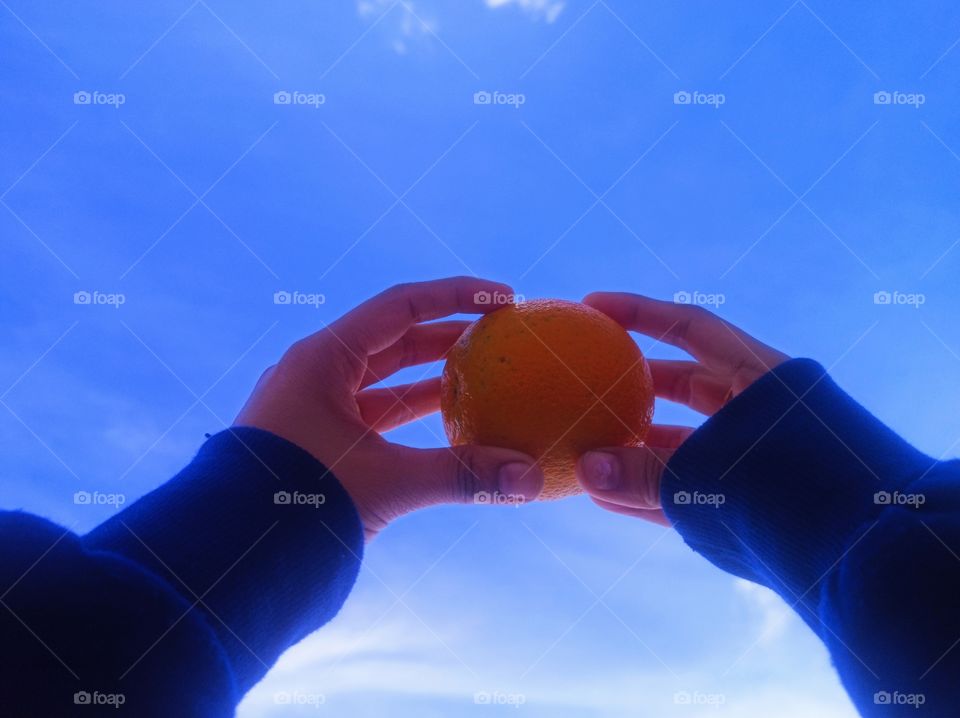 an adult woman is holding orange in her hands up to the sky