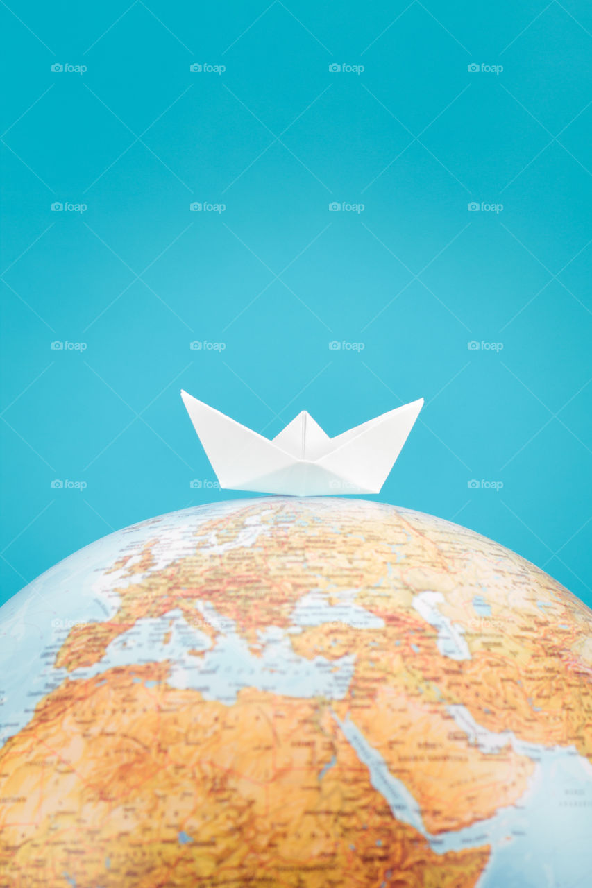 Go around the world. Paper ship over the globe on plain blue background