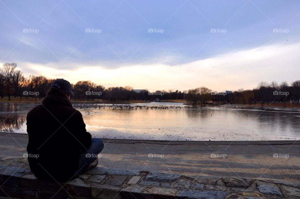 Man sitting on the ground looking at frozen lake