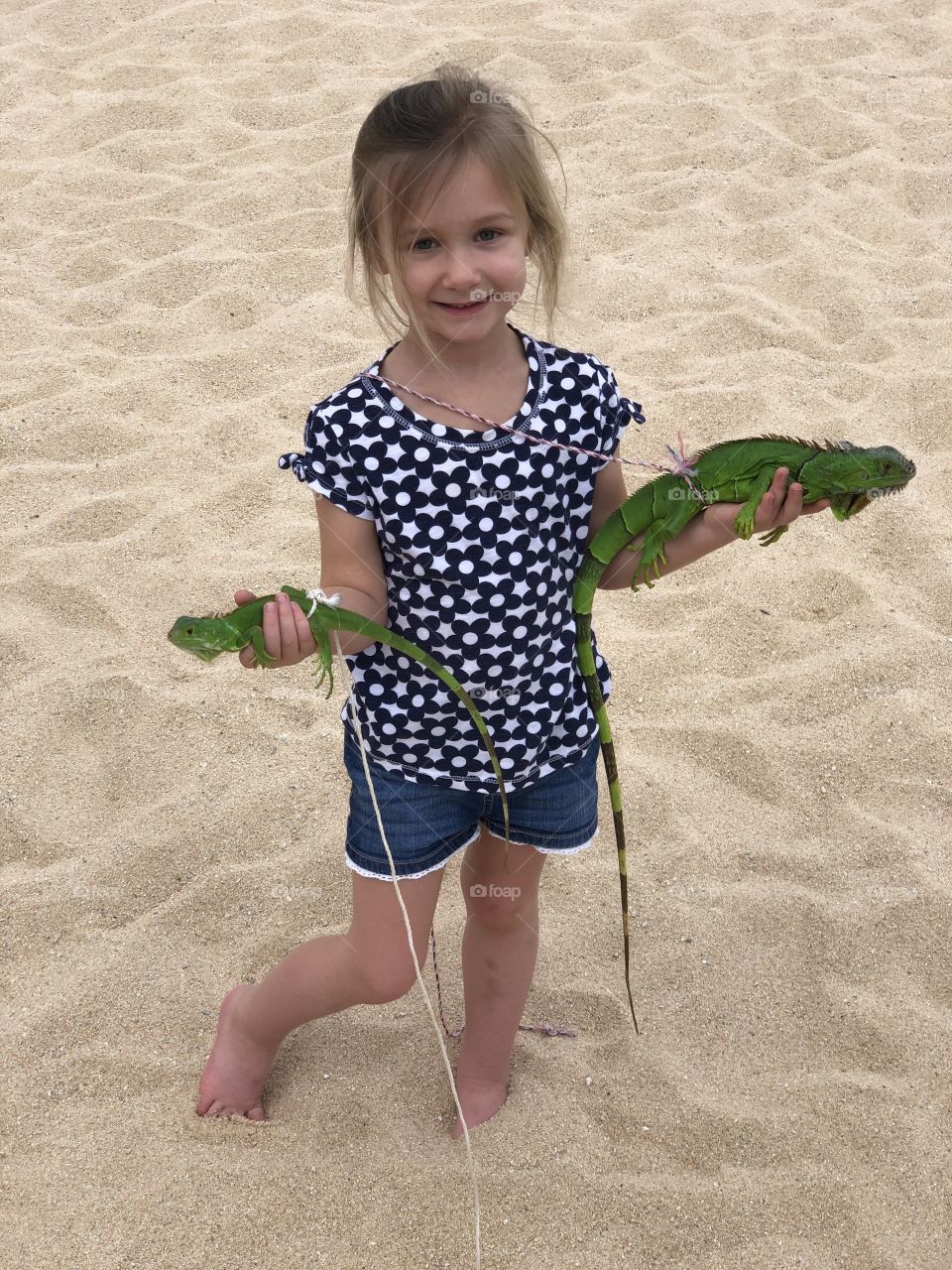 Little girl standing in the sand holding green iguanas