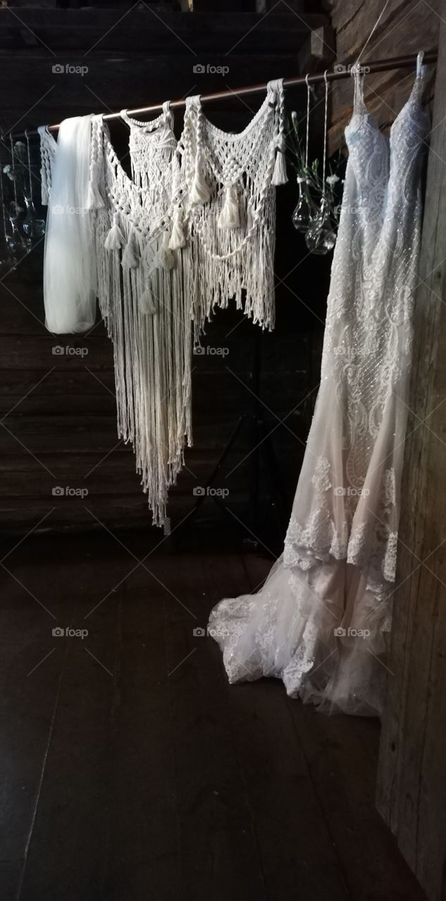 The wedding dress is hanging next to the macrame and the glass bottles with the white carnations.