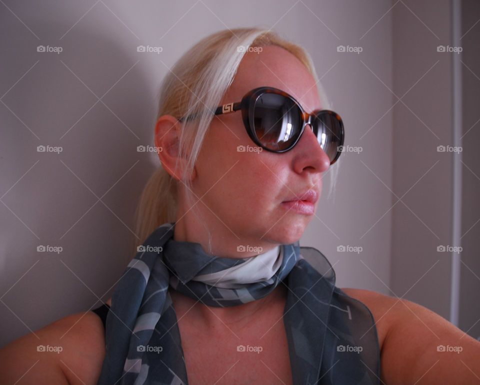 Unas gafas de sol de una famosa marca de moda cubre la cara de la mujer de la foto , su pelo rubio está recogido en una discreta coleta . Su cuello rodea un pañuelo en tonos verdosos y grises de seda oportandole un toque de distinción.