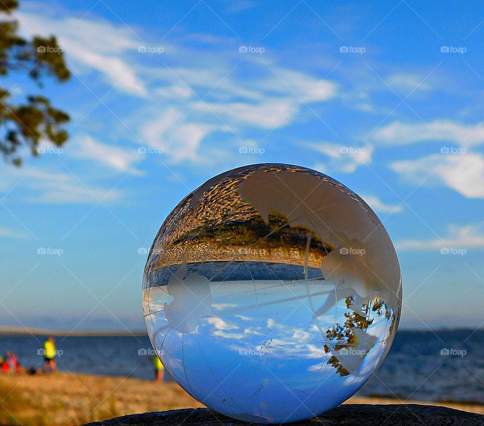 Looking at the beach, the people on the beach,  the blue sky and clouds through a crystal ball 