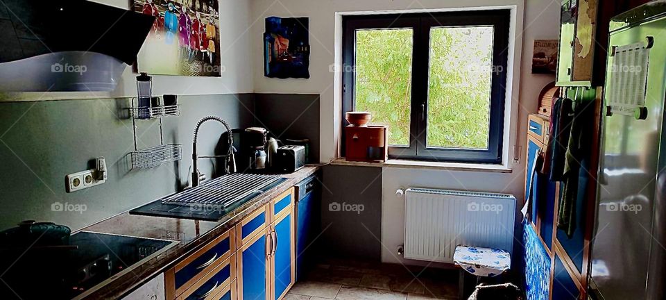 This is the kitchen of the house in „Bavaria“, Germany looking out the window onto the front yard and garden. There is a large steel sink, cabinets and a grain mill to make fresh muesli for breakfast. 2023. Hypnotic Productions