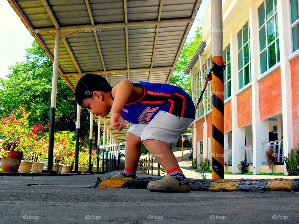 little asian boy playing under the shade of a covered hallway