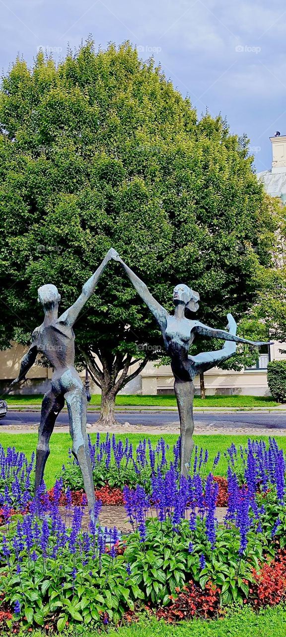 A statue of a dancing couple, a man and a woman in the prime of their lives with the strength and grace a human being can have in a beautiful park in the city of “Ystad” by the “Baltic Sea” in “Sweden” reminds of paradise. 2023. Hypnotic Productions