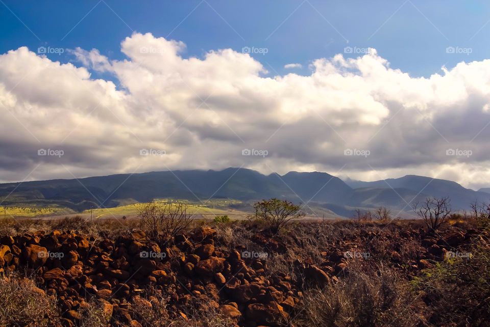 Beautiful landscape view on the island of Maui in Hawaii, stunning clouds with deep red rocks in the foreground. A perfect island day