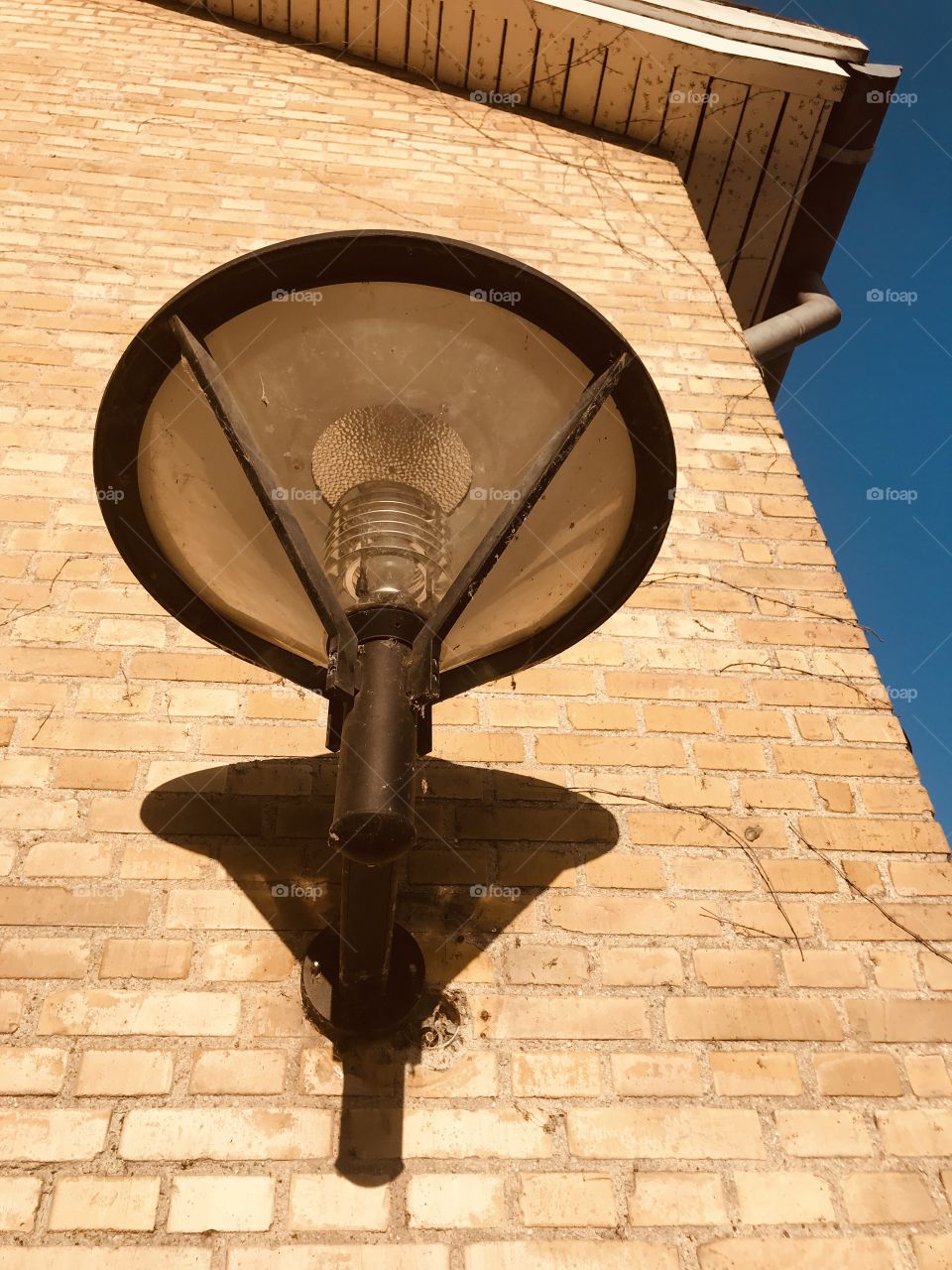 Street lamp in the sunlight casting shadows on the brick wall