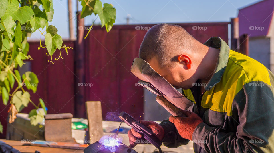 Welder weld metal with an electrode looking at the seam through a welding mask