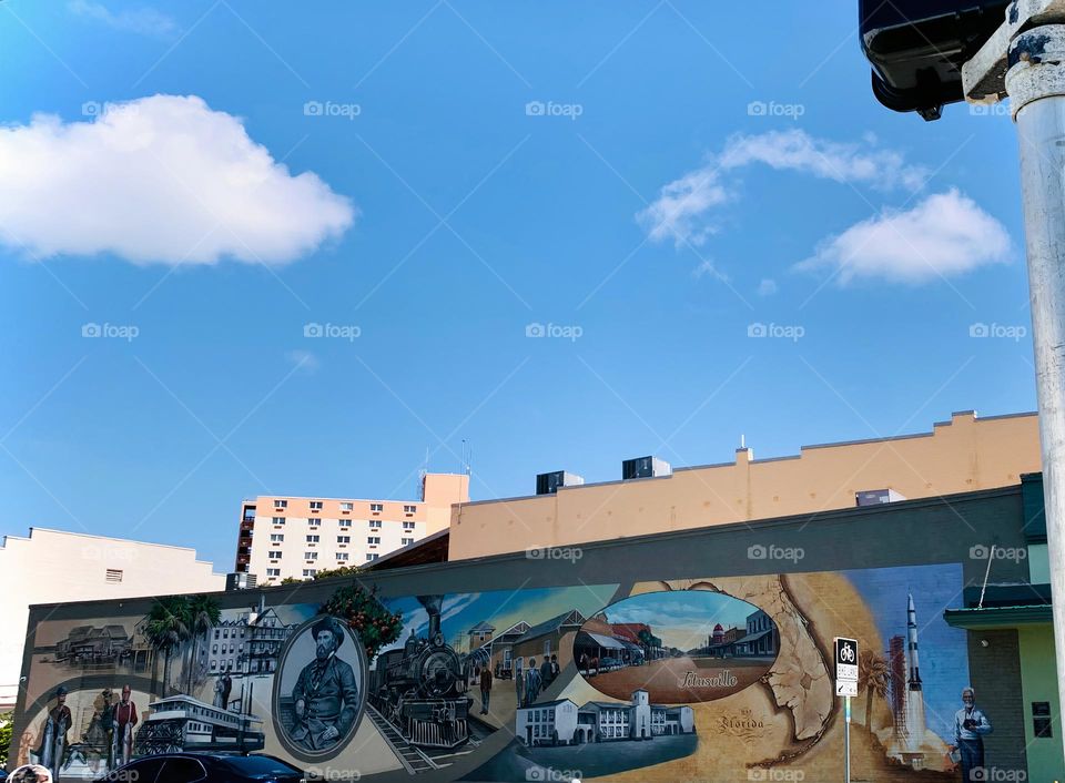 Historical story of Titusville town shown in painting on a building wall downtown with large white and beige apartment building on the background and stairs steps roof type old architectural white building beside it.