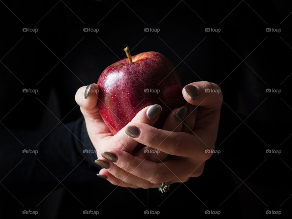 Hands holding a red apple with a black background