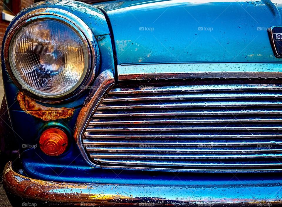 Front end of a car, classic cars in England, fresh rain on a car bumper, portrait of headlights, car grill 