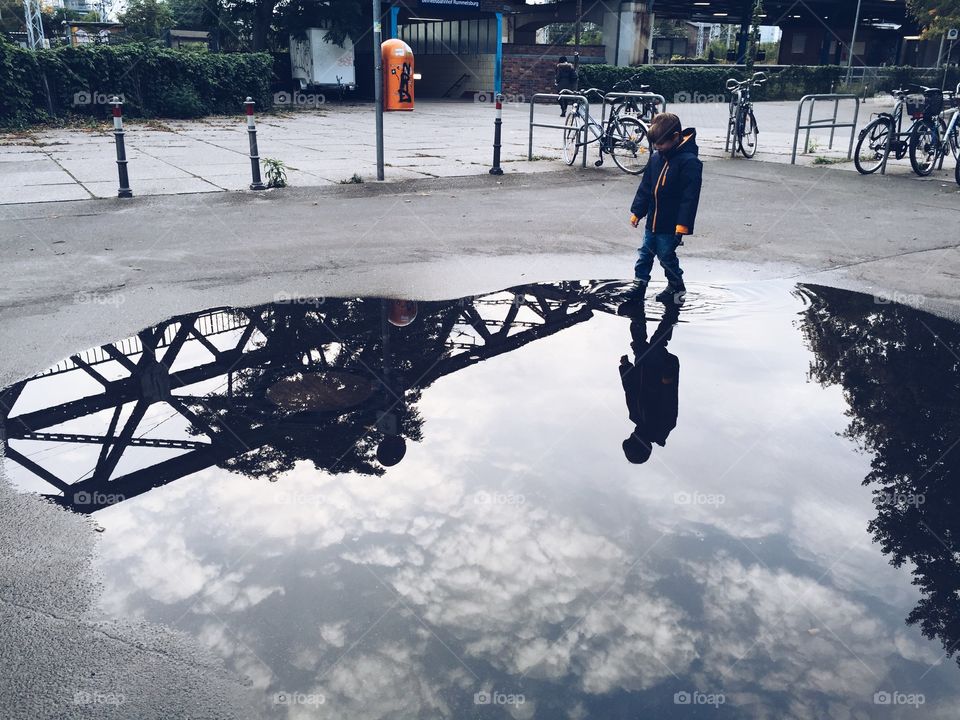 Boy going through puddle. Boy walking through huge puddle with reflection of sky