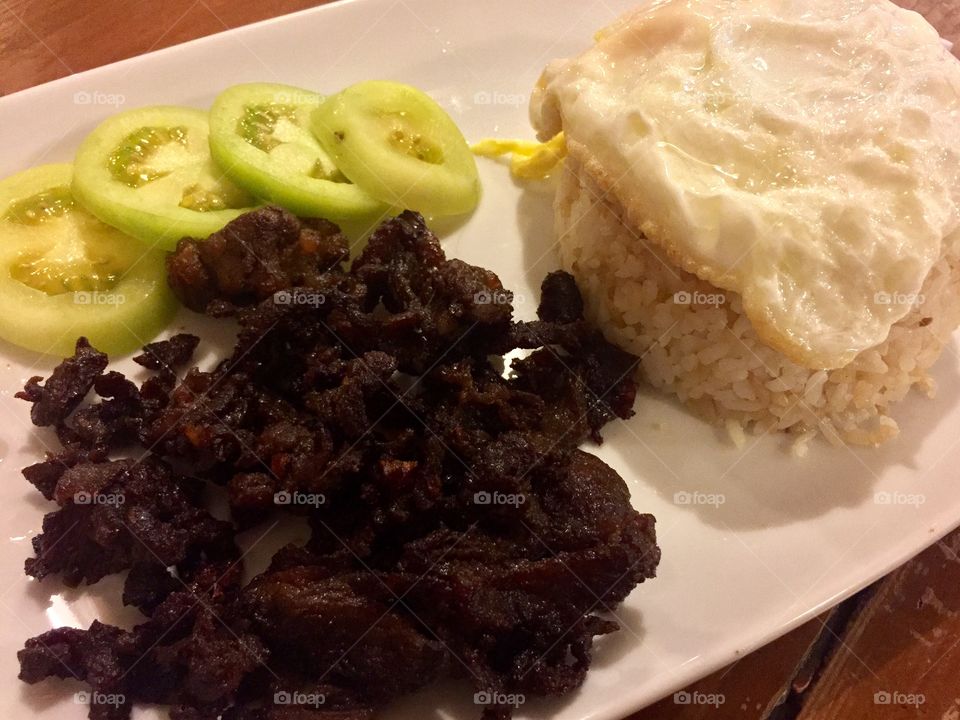 Beef tapa served with slices of fresh tomato and fried egg on top garlic fried rice.