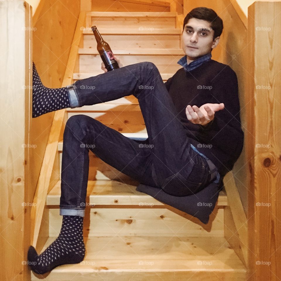 Man  with a bottle of beer asking and sitting on steps of a wooden stairway in cottage 