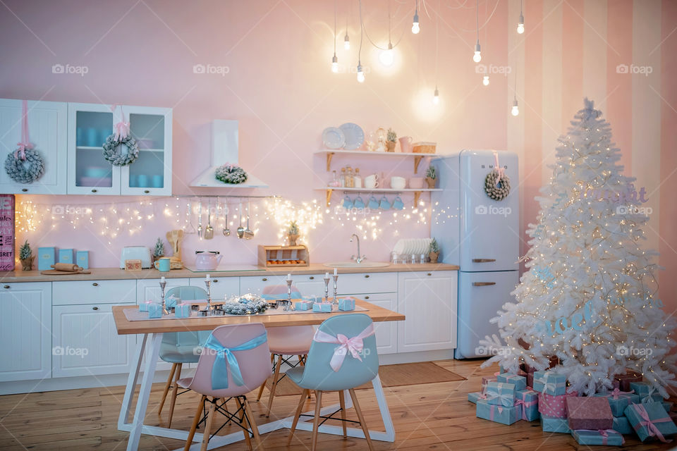 Festive winter cozy kitchen interior with garlands, decorations and gifts.  Christmas dinner at the decorated table.