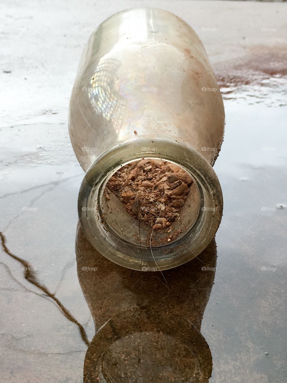 Antique milk bottle freshly dug up discovered laying on side in rain reflection in water 