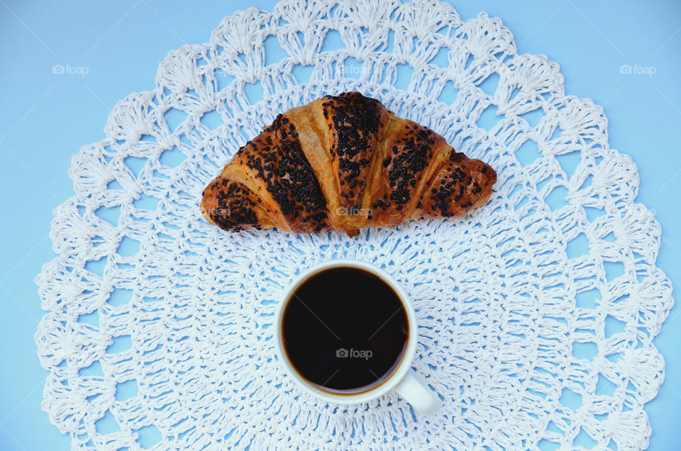 Business working morning with cup of hot coffee, fresh delicious croissant on blue background close up. Top view, copy space, flat lay, mockup.
