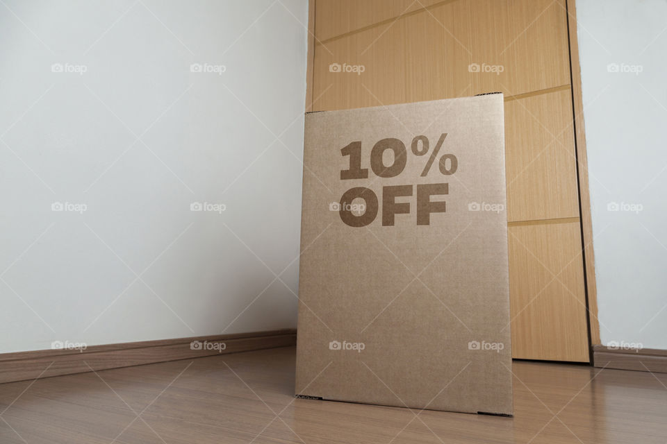 Cardboard box with 10% off order written on the box placed on the floor in an empty room with a neutral background. delivery concept. economy concept. business concept. shopping concept. copy space.