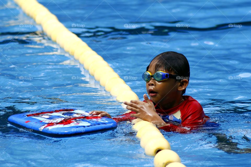 a young boy with goggles and kick board in a swimming pool
