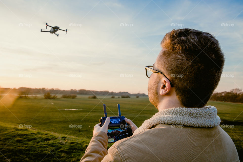 A male drone pilot flying a drone using a remote control at sunset