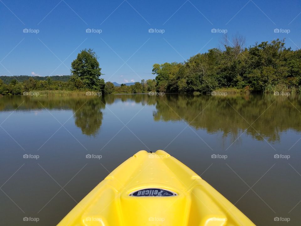 yellow Kayak on smooth lake with trees and sunny blue sky