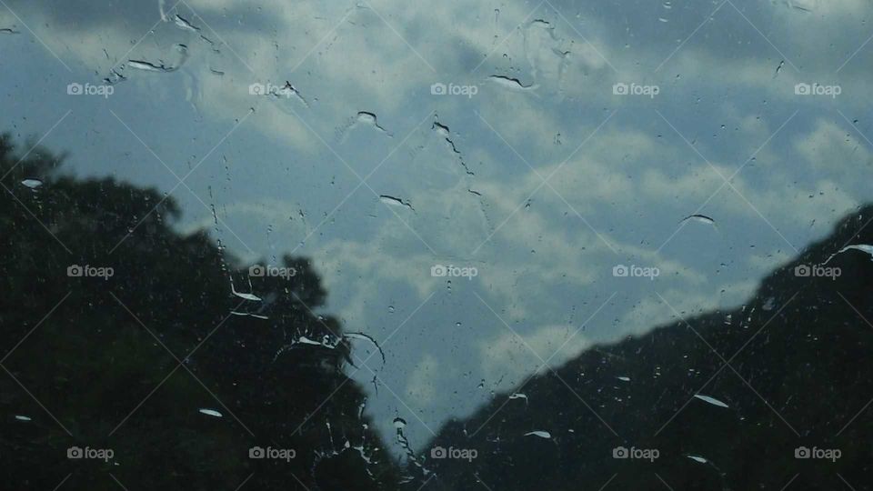 Raindrops on a windshield with mountains and clouds behind.