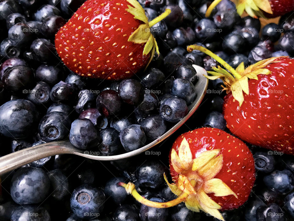 Red ripe strawberries and blackberries in the spoon