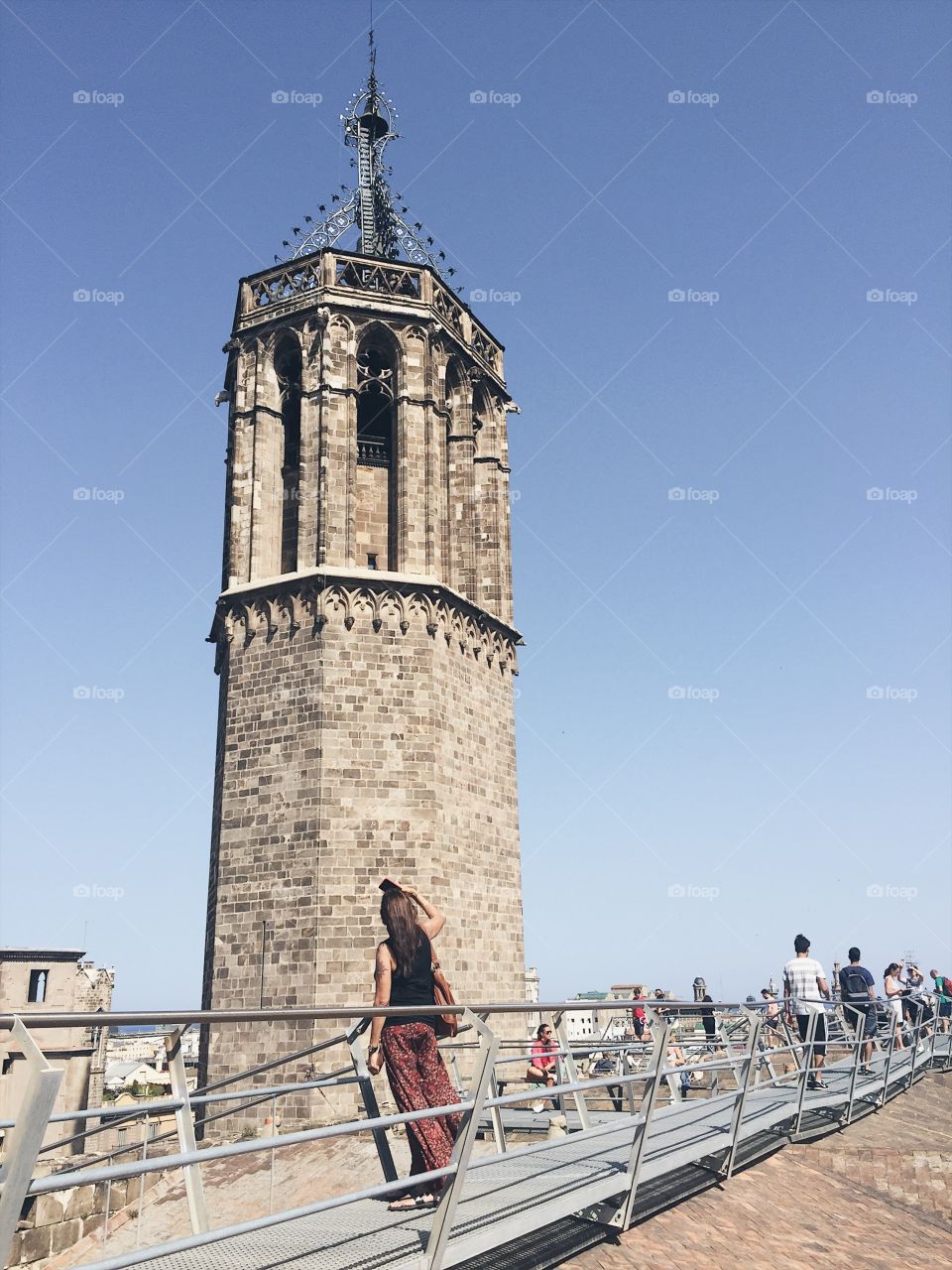 The view from the top of a historic cathedral in Barcelona, being enjoyed by several tourists on a sunny day with clear skies.