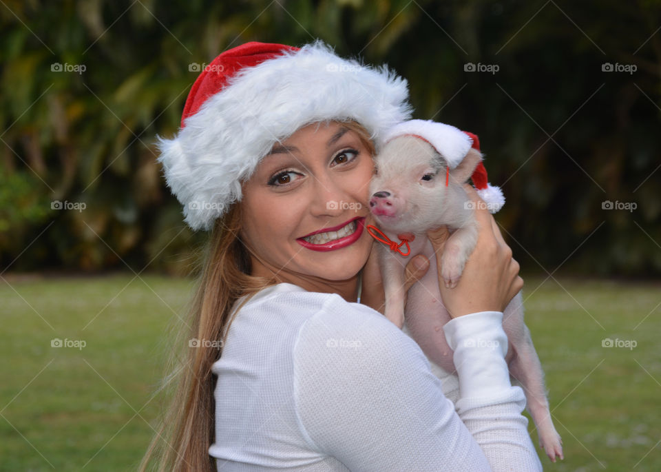 Young woman holding piglet with christmas cap