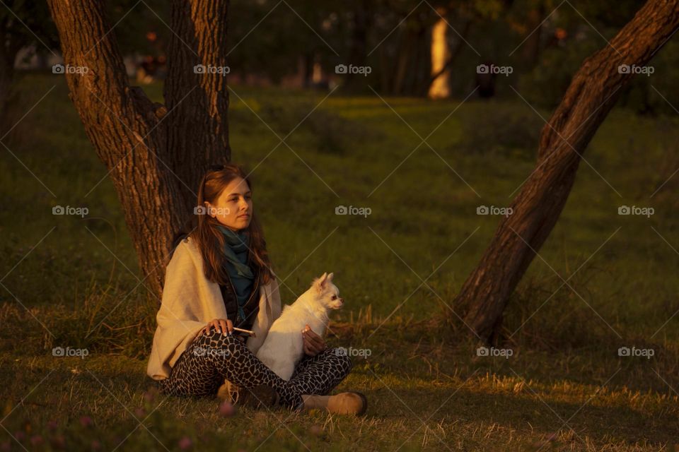 Young woman with white dog siting in autumn park at sunset.