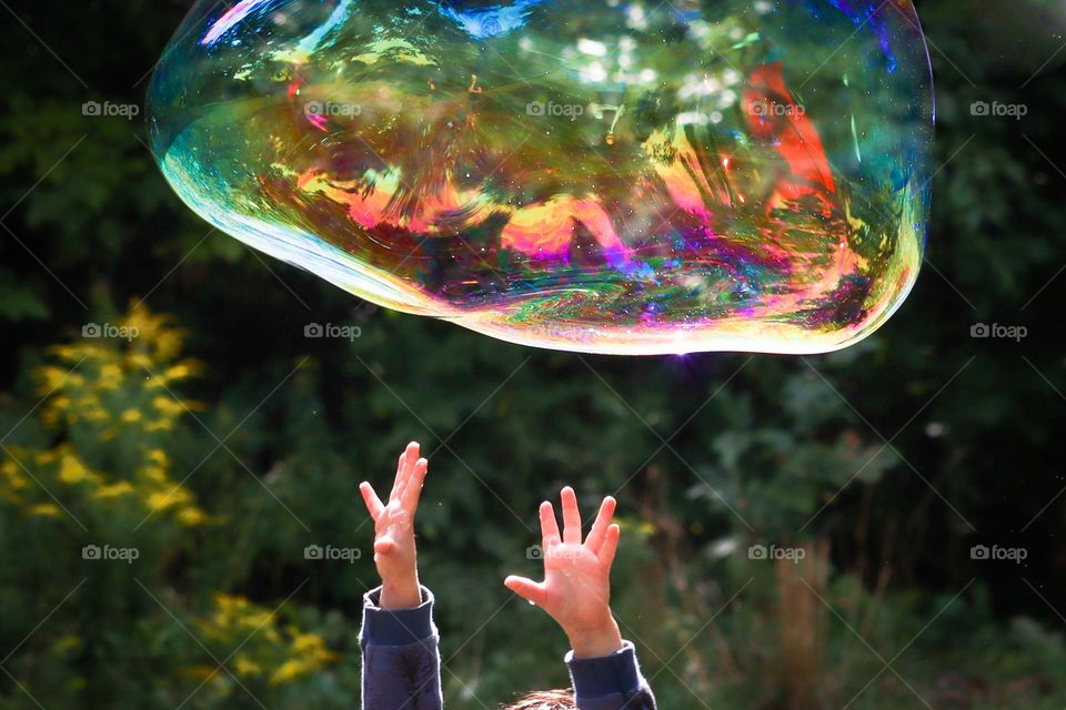 Cute child's hands are trying to reach huge soapy bubble