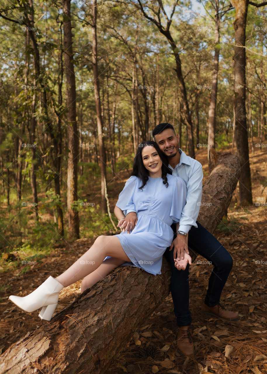 Couples of young people sitting in middle of the forest while looking smiling and happy, in a sunny day.