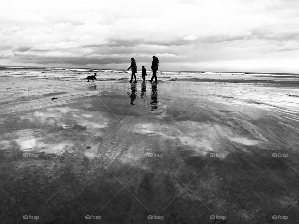 Family stroll on the beach with the dog leading the way ...