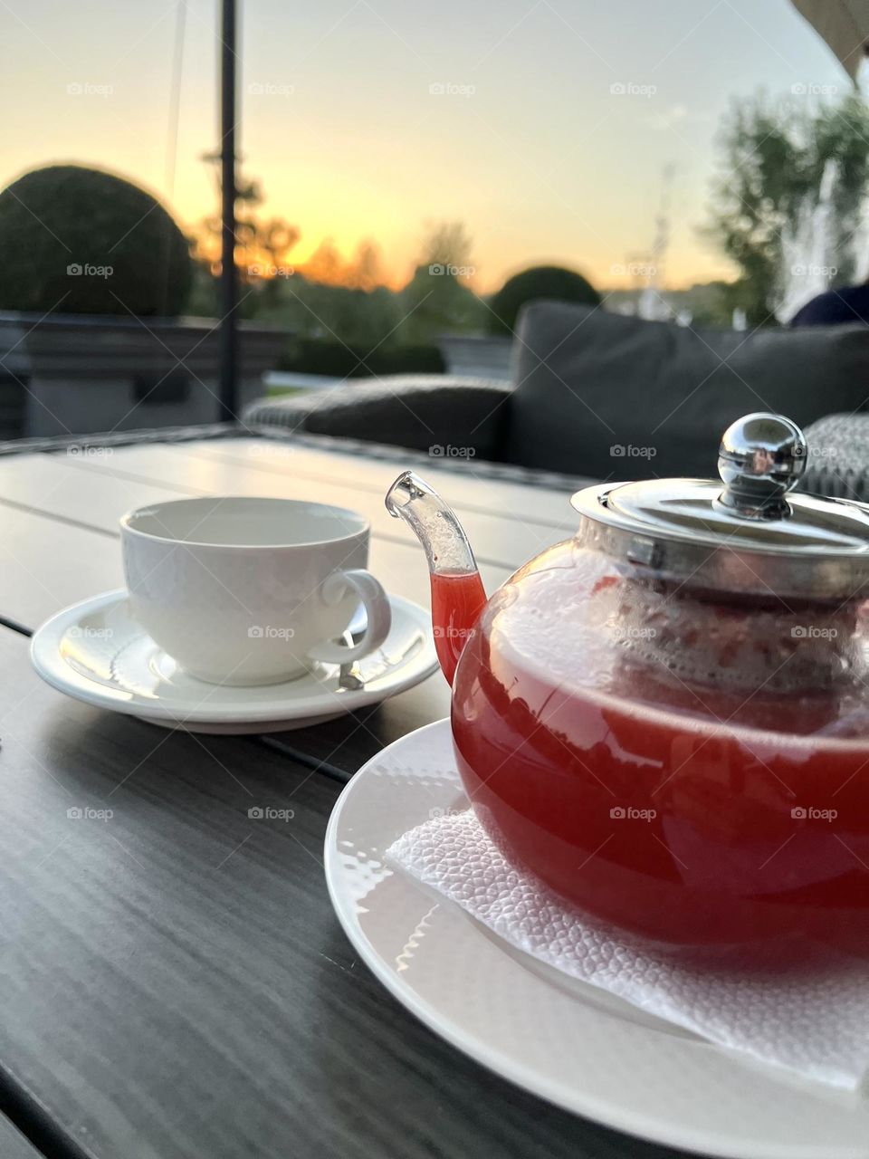 Волшебный закат окутывает небо в красках огня, создавая идеальное обрамление для вечернего чаепития.На заднем плане утопает солнце,распуская последние лучи нежности.Пар стоит над чашкой чая, приглашая вас насладиться моментом 
