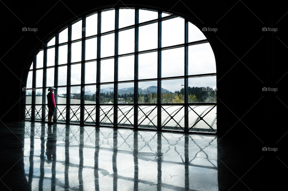 Looking out the window. Silhouette and reflections of a woman looking out a big window