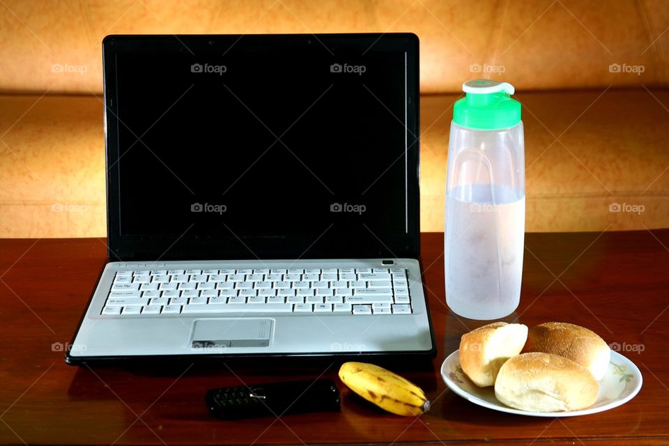 laptop computer, tablet, cellphone, smartphone, banana, bread and water on a living room table