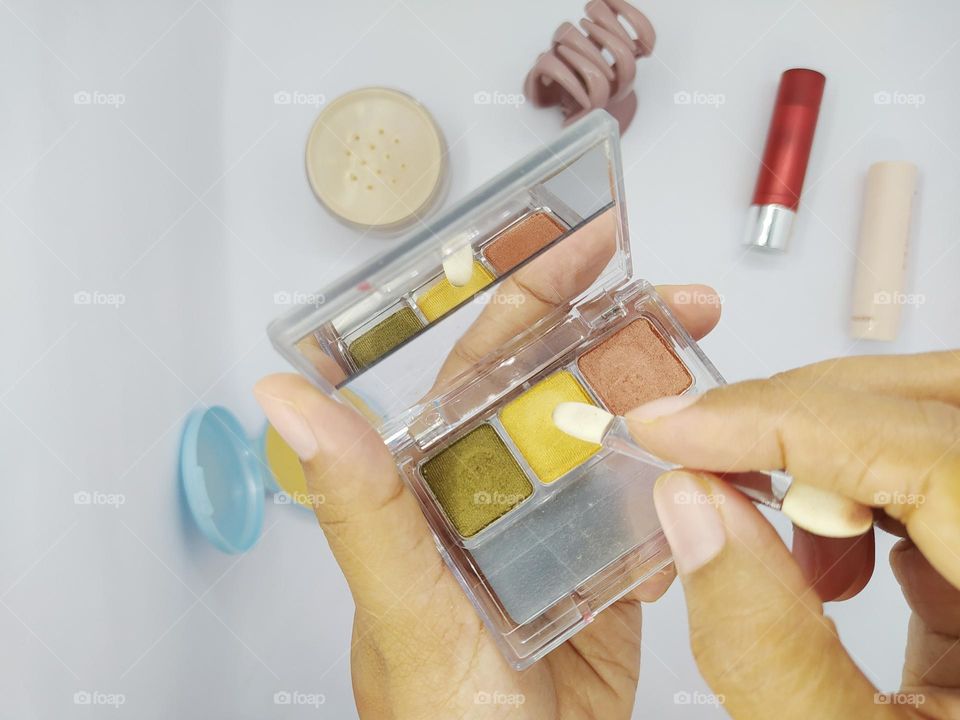 The hand holding the eyeshadow kit applicator.  makeup tools on a white background